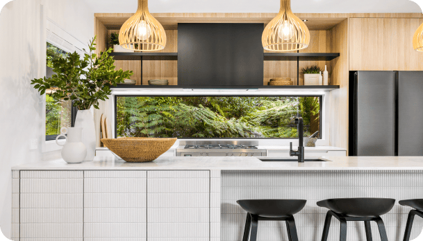 Auckland Home Builders Modern kitchen space with appliances and kitchen island with three bar stools.